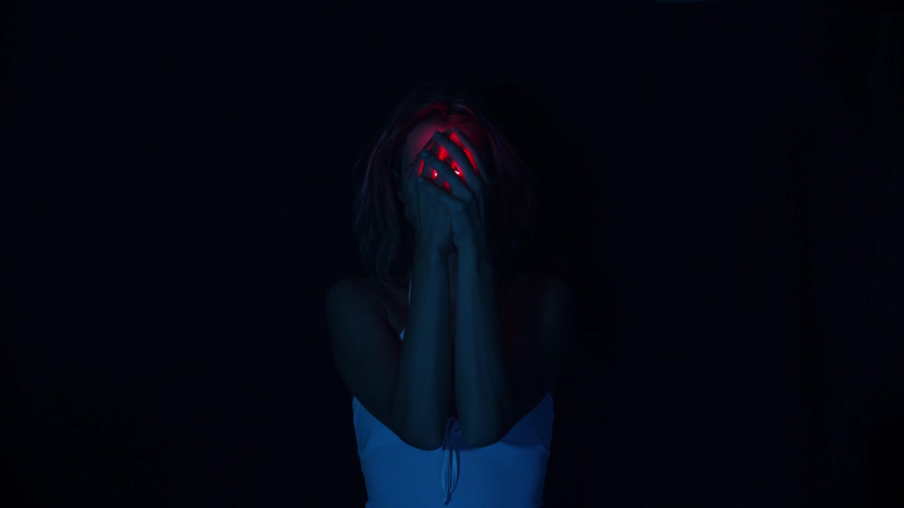 Woman holding a red neon light bulb hiding her face