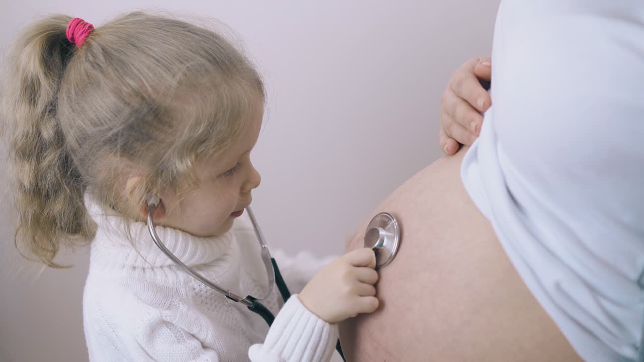 una ragazza con uno stetoscopio ascolta il bambino nella pancia di una madre incinta