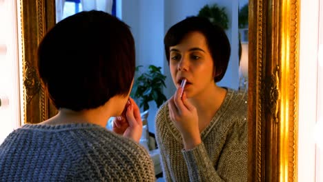 mujer aplicando lápiz labial mientras mira al espejo