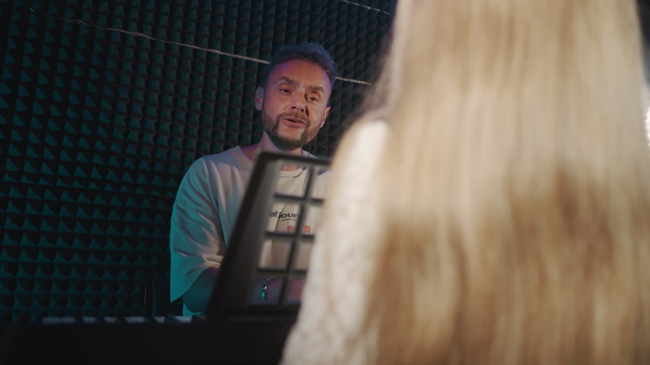 Instructor sings with child in recording studio. Fair-haired small girl practices vocal rendition while teacher plays musical instrument during lesson