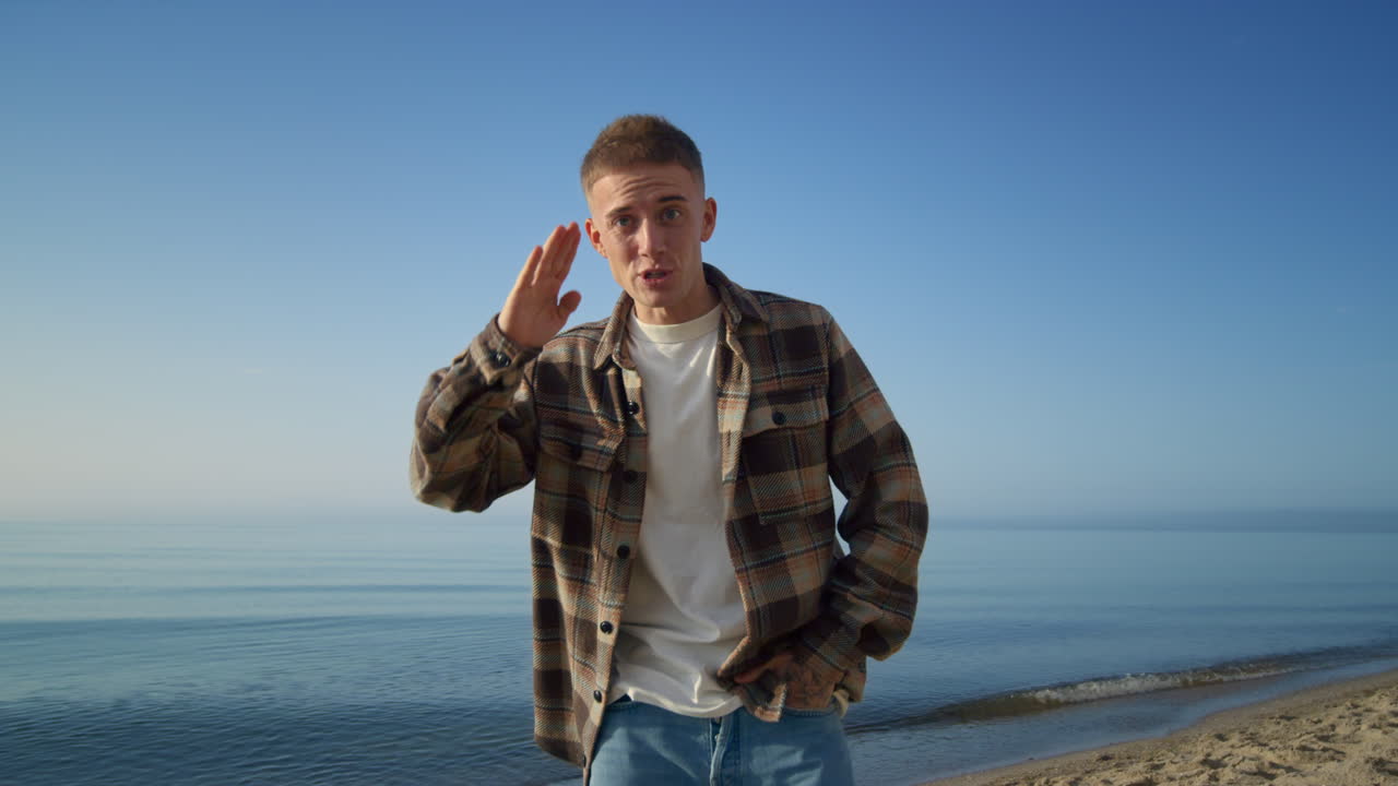 hombre feliz acercándose a la cámara vlogging en la hermosa orilla del mar mañana soleada.