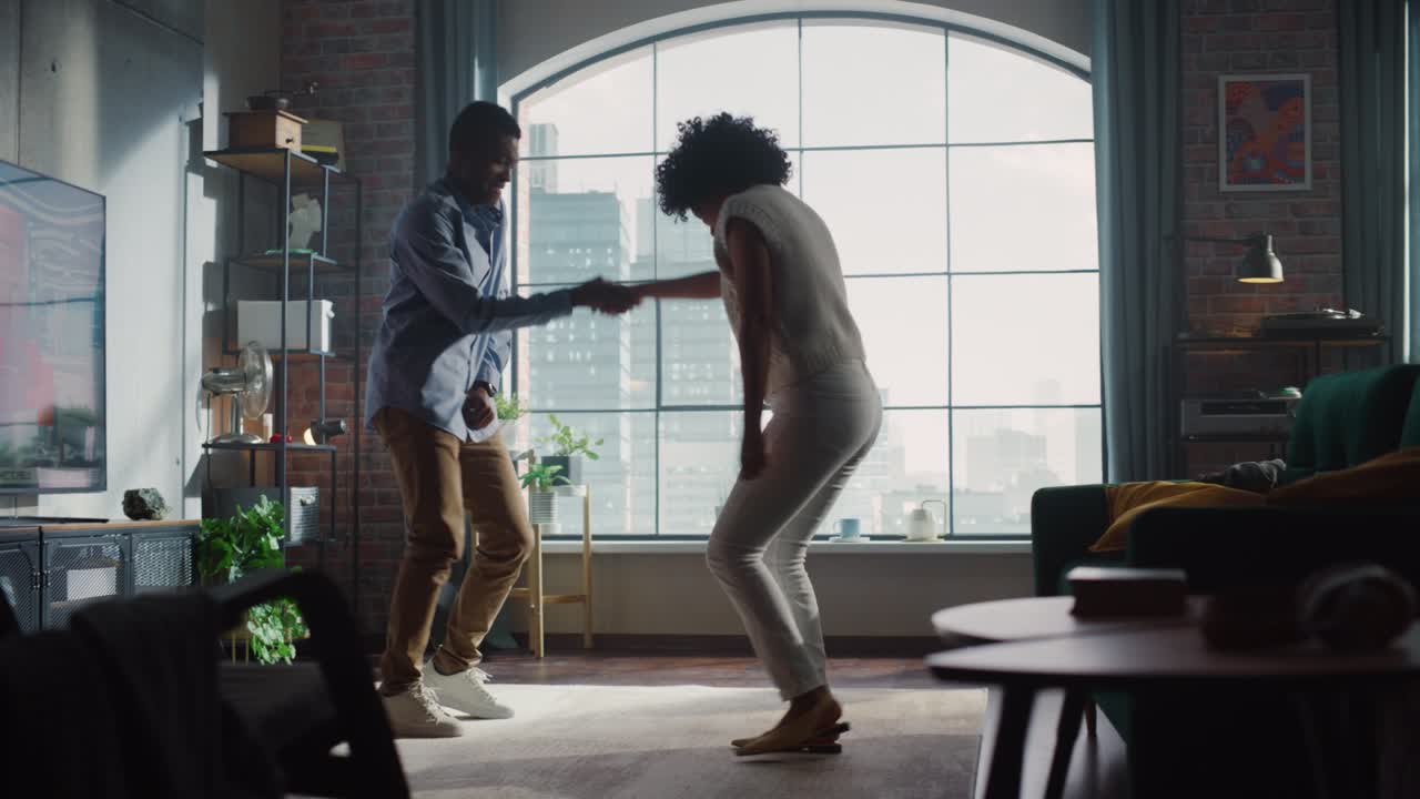 Beautiful Stylish Multiethnic Couple in Comfy Home Clothes Dancing and Enjoy Life at Home in Loft Apartment. Boyfriend and Girlfriend Cheerfully Celebrate by Dancing at Home