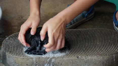 Mujer-Asiática-Lavando-Ropa-A-Mano,-Lavando-Ropa-En-Una-Antigua-Tabla-De-Lavar-Pedregosa-Fuera-De-Casa-En-Un-Pueblo-Coreano---Cerrar-En-Cámara-Lenta---Las-Manos-De-Una-Mujer-Se-Cierran