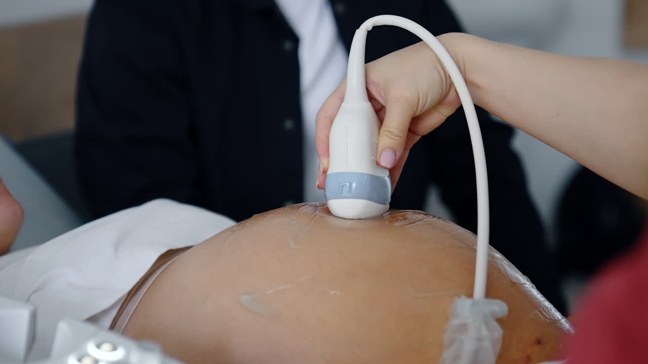 Female doctor's hand moves the ultrasonic device by the big round belly of pregnant lady. Close up. Pregnancy examination.