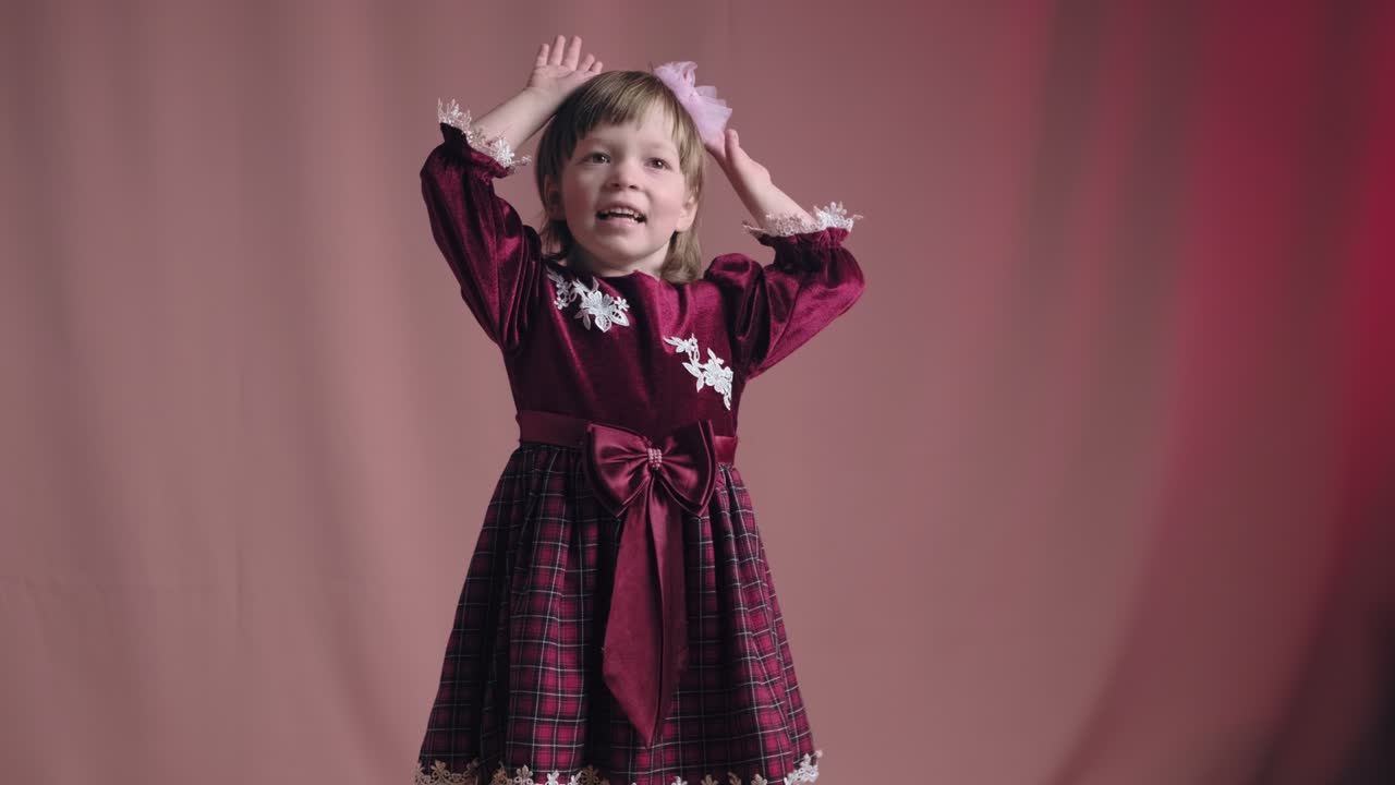 Little girl in vintage burgundy dress is dancing, rejoicing, making funny faces