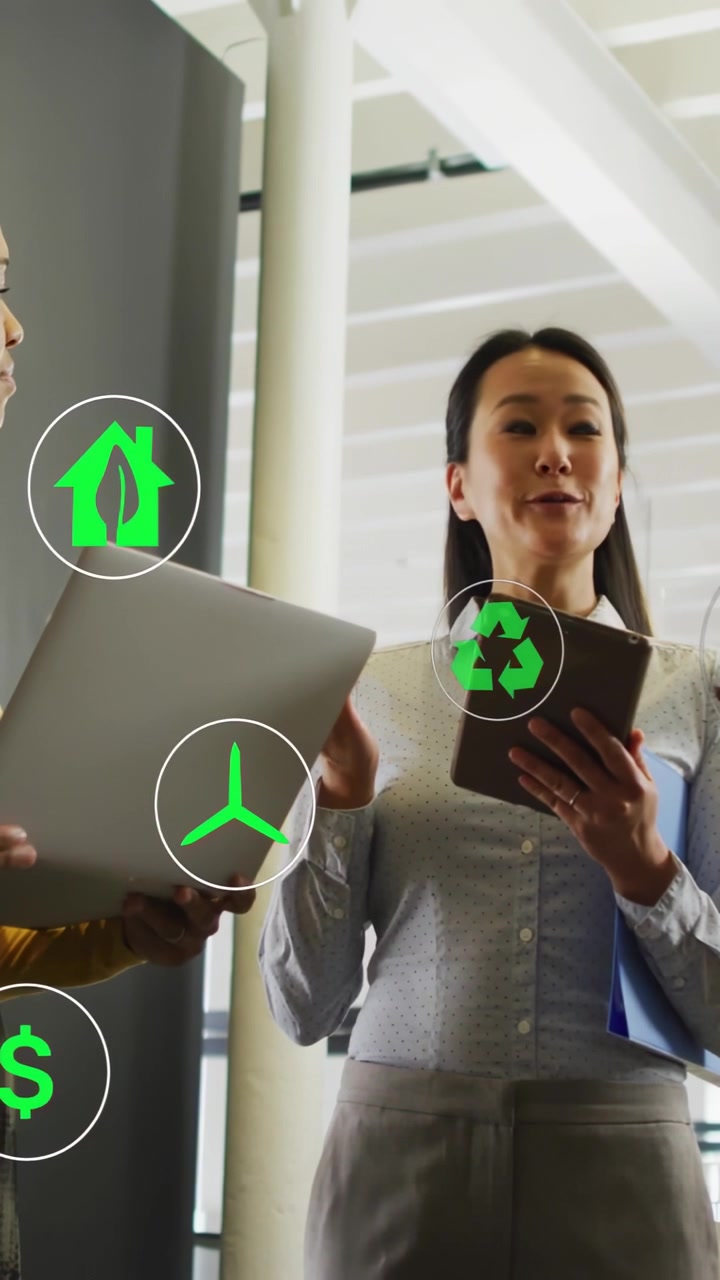 Video vertical: Mujer usando una tablet y un colega usando un portátil, revisando finanzas verdes con iconos flotantes.
