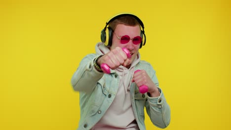 sporty teen student man listening music via headphones, working out, pumping up lifting dumbbells