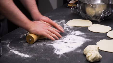 a shot of a man kneading bread dough on a black big table at the evening, preparing food for family, close up shot