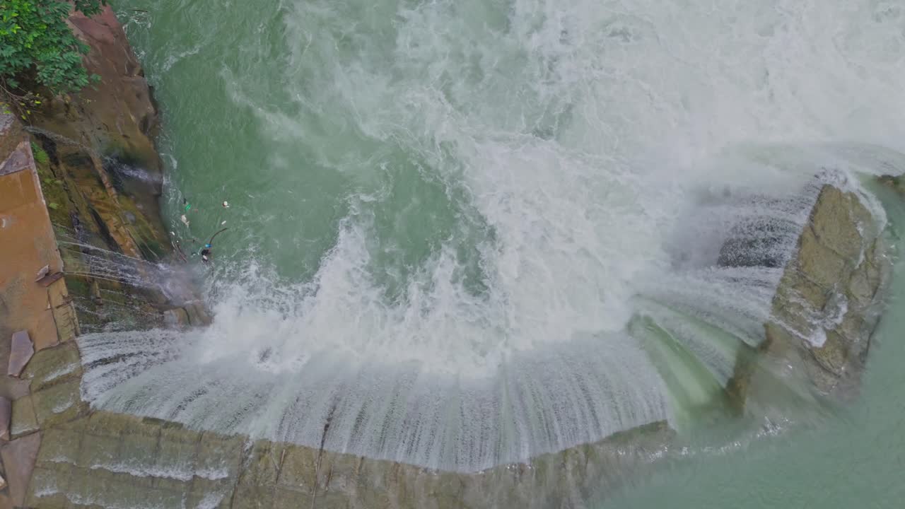 Aerial drone view of a beautiful waterfall merging into a flowing river, capturing the natural beauty of water movement, rocky terrain, and pristine landscape