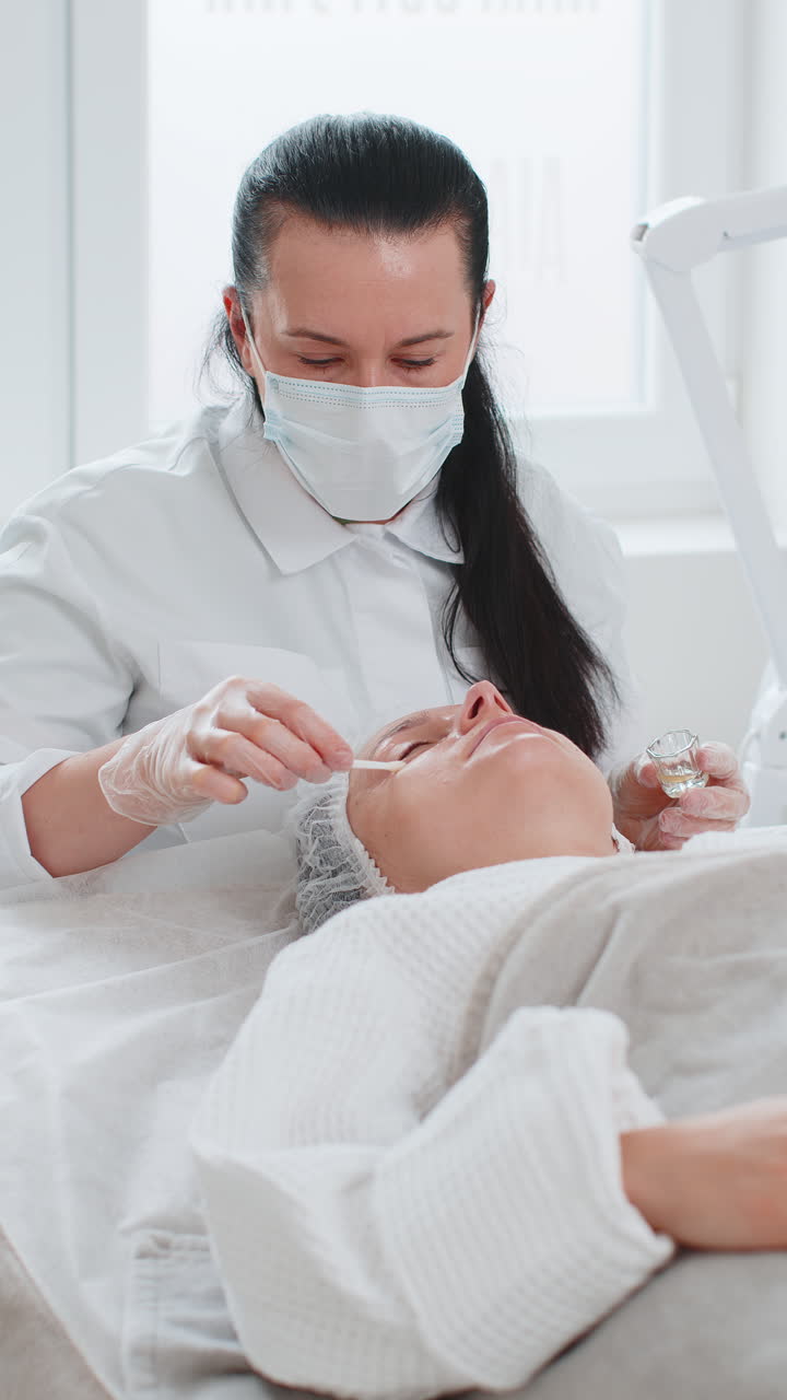 Cosmetologist applying moisturizing peeling acid on skin around eyes of woman antiaging treatment