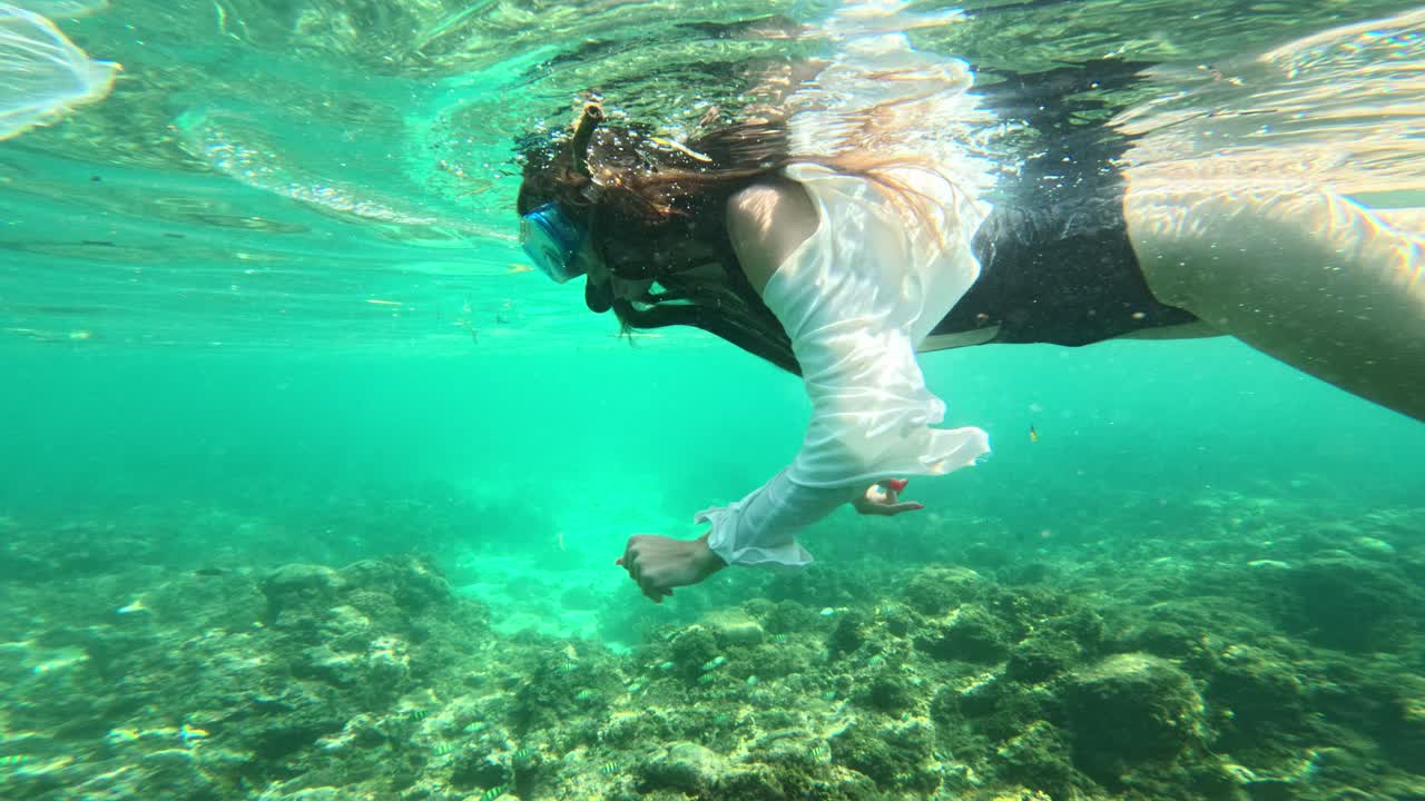 Donna in costume da bagno e maglietta che fa snorkeling sulla barriera corallina in acque tropicali turchesi.