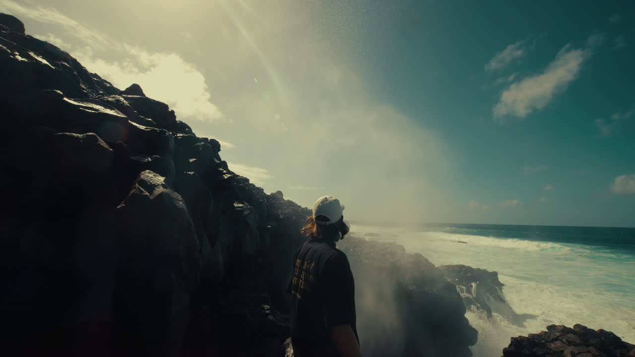 Man looking at powerful waves crashing on volcanic coastline