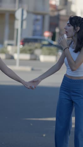 two young women holding hands and walking on an urban street