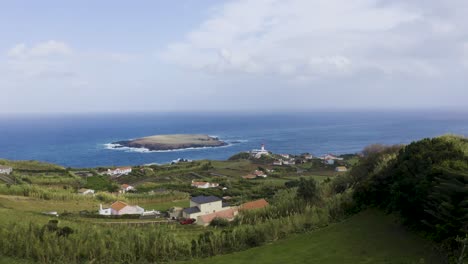 Pueblo-Costero-Rural-Con-Un-Faro-Y-Una-Isla-En-El-Océano-Atlántico,-Cielo-Nublado-En-Topo,-Isla-De-São-Jorge,-Las-Azores,-Portugal