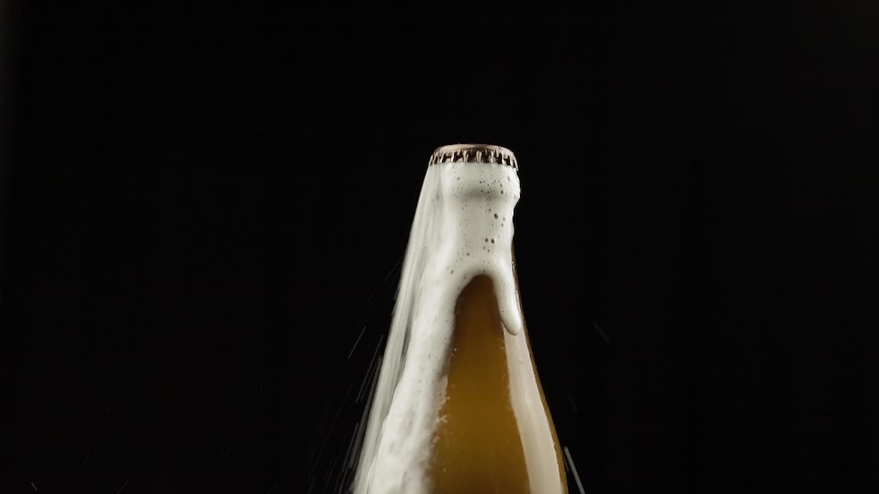 Uomo scuote una bottiglia di birra. La birra inizia a fuoriuscire con schiuma da sotto il tappo