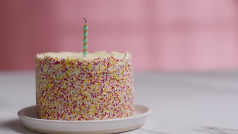 single candle being blown out in studio shot of birthday cake covered with decorations 1