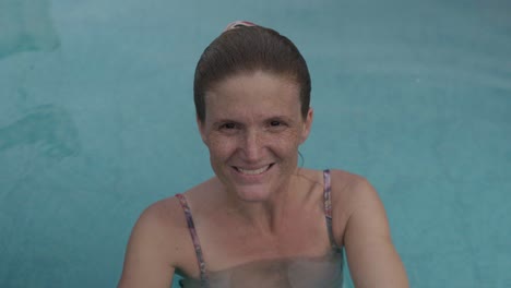 a young redhead woman inside a swimming pool smiling at camera