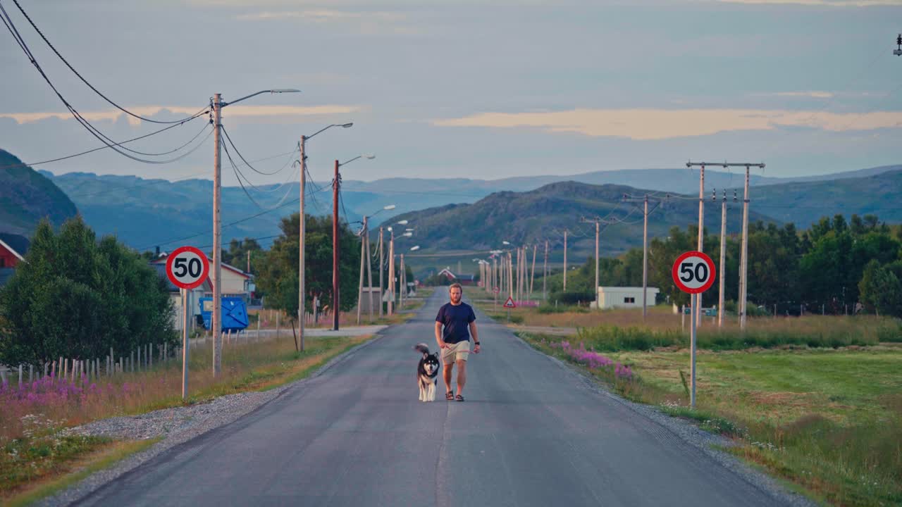 Man With His Dog Walking In The Middle Of The Road. - wide shot