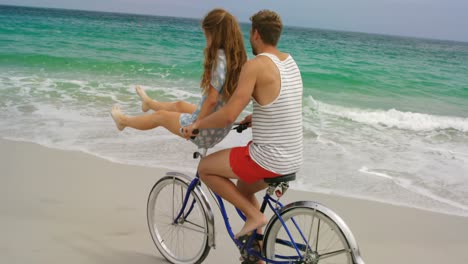 vista lateral de una pareja caucásica montando una bicicleta en la playa 4k