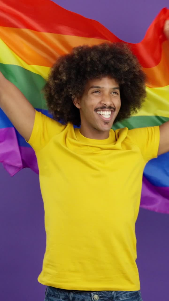 Smiling man with an afro holding a rainbow pride flag