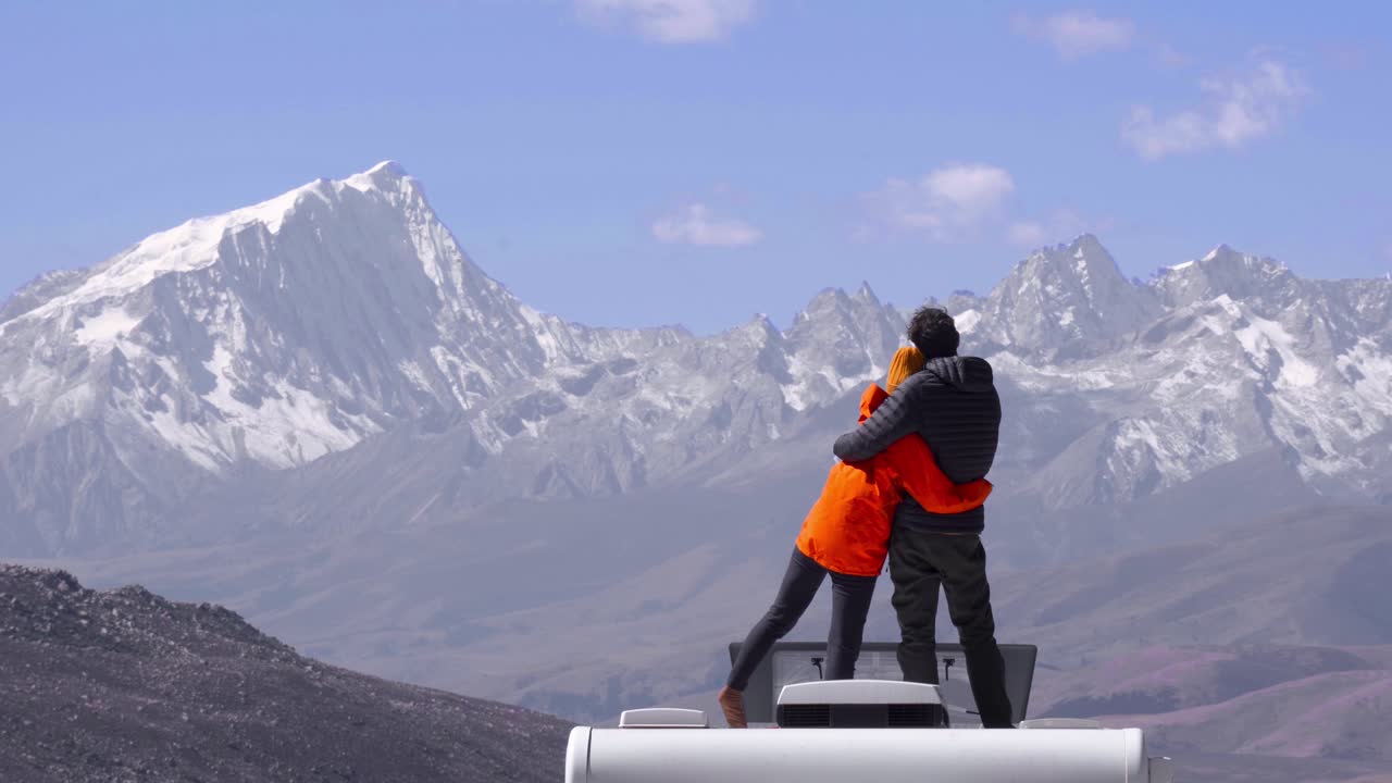 pareja de abrazos y abrazos en la parte superior del techo de la caravana mientras exploran las montañas nevadas de sichuan