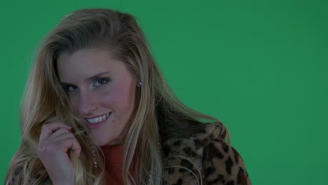beautiful blonde woman in leopard print coat smiles at the camera in front of green screen