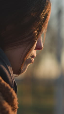 una chica llorona caminando por un parque al atardecer, con un abrigo marrón y una sudadera con capucha. el primer plano enfatiza su estado emocional, con la luz suave y dorada que cubre su rostro