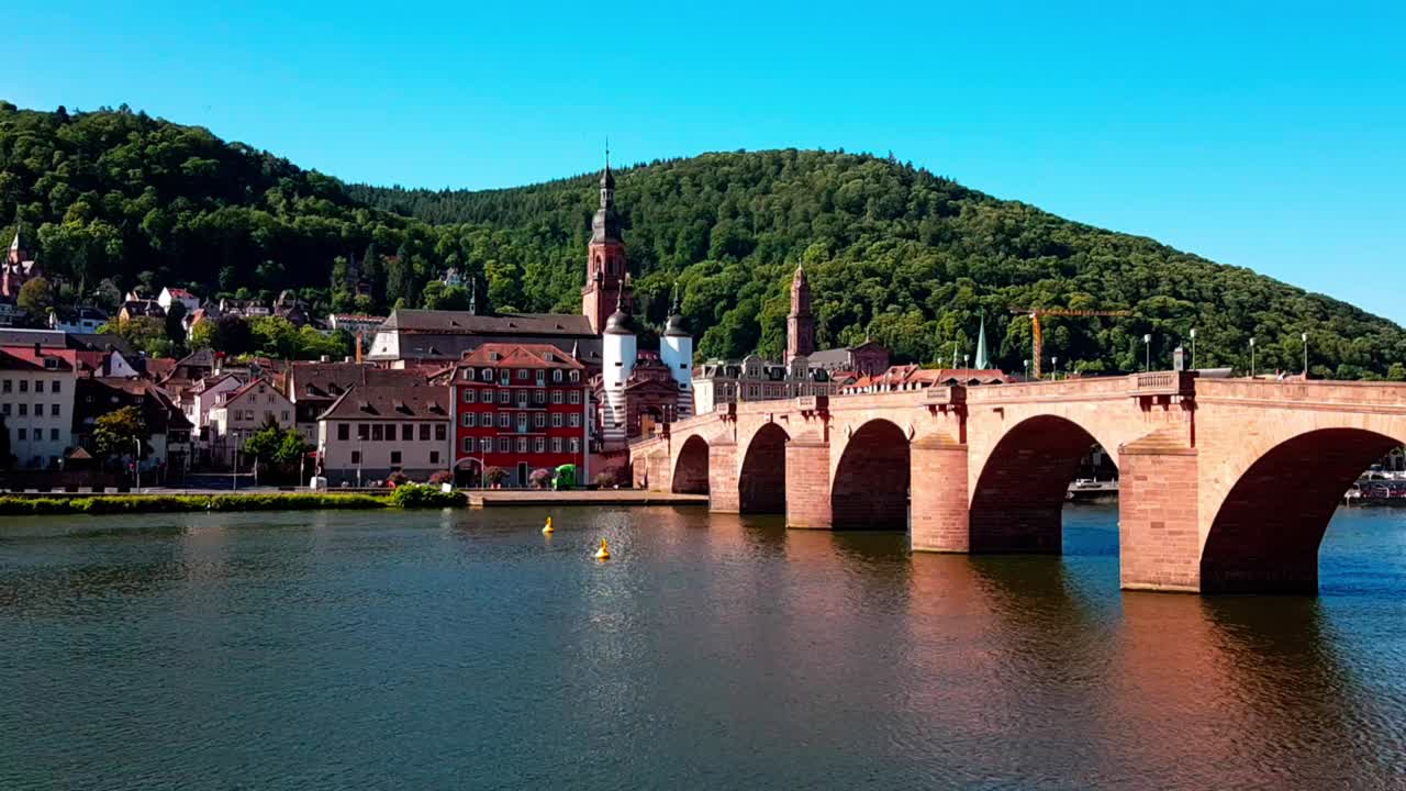 Static view of beautiful old brown bridge with river running under it, traffic in background, Heidelberg Germany