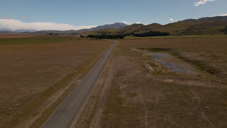 Aerial-tracking-shot-of-distant-car-driving-along-rural-countryside-highway-in-sunny-prairies