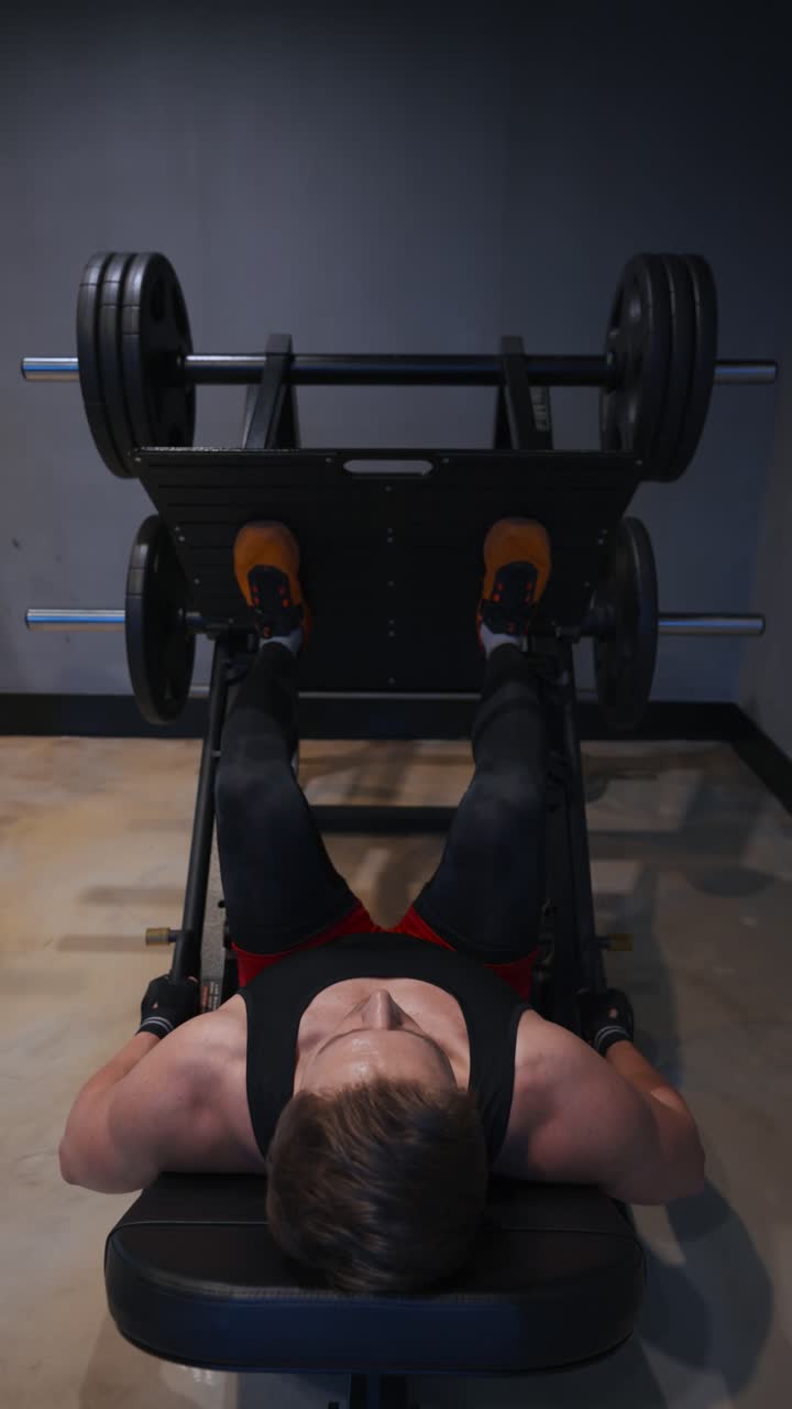 Vertical - strong muscular man performing a heavy leg press exercise on a machine, building leg muscles during a gym workout
