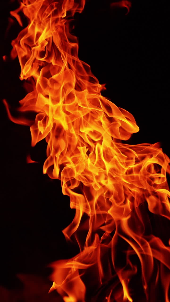 Wooden logs stacked in a pile burn in a big bonfire. Fire flames bending to the right in darkness. Vertical video
