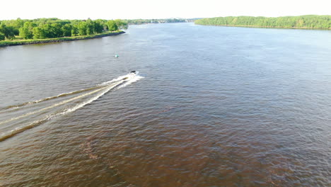 Speed-boat-booking-it-down-the-Delaware-River-on-a-spring-evening,-revealing-Burlington-Bristol-Bridge