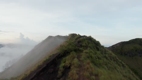 Tiro-De-Carro-Aéreo-Ascendente-Volando-Más-Allá-Del-Pico-De-La-Montaña-De-Un-Monte-Batur-En-Bali-Cubierto-De-Vegetación-Tropical