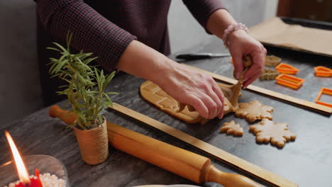 close up of woman hand removing cutout dough shape carefully from rolled dough with orange cutter decoration near candlelit cozy kitchen table setting wooden roller pin