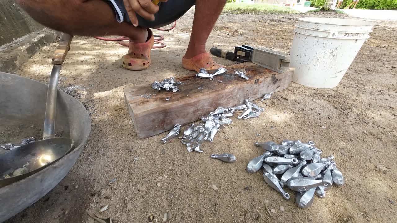 Person making lead sinkers on a sandy surface, daylight, handcrafting, close-up