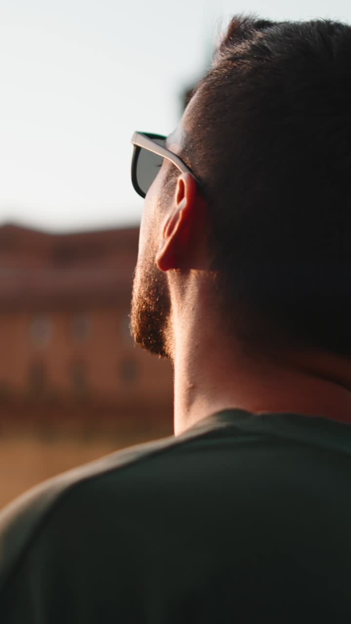 Man with beard and sunglasses looking up at a building