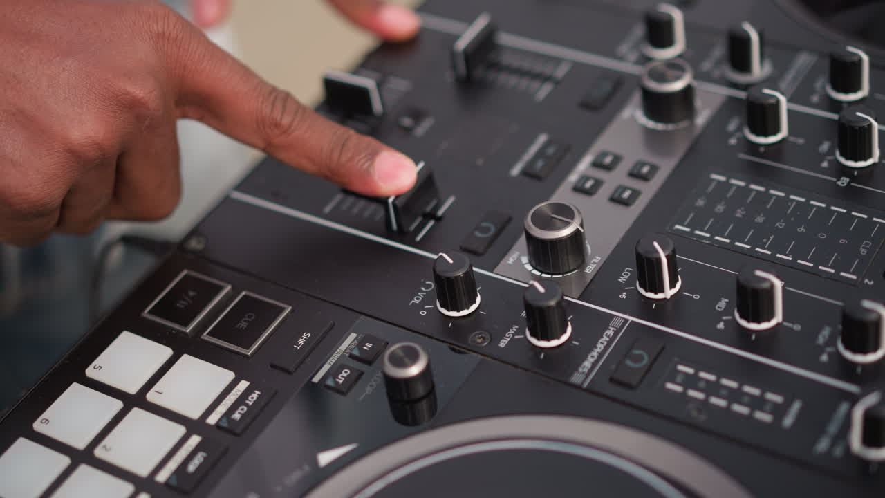 Primo piano delle mani di un DJ nero sul mixer, performer da club che regola crossfader e manopole, precisione delle dita sul controller, vibrante energia della vita notturna, folla suggerita, movimento ritmico, soundcheck sul palco, dal vivo.