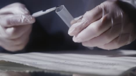 a forensic detective's hands take a sample of paper or ink with a scalpel