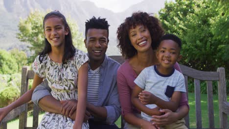 padres africanos americanos felices, hija e hijo sentados al aire libre en un banco