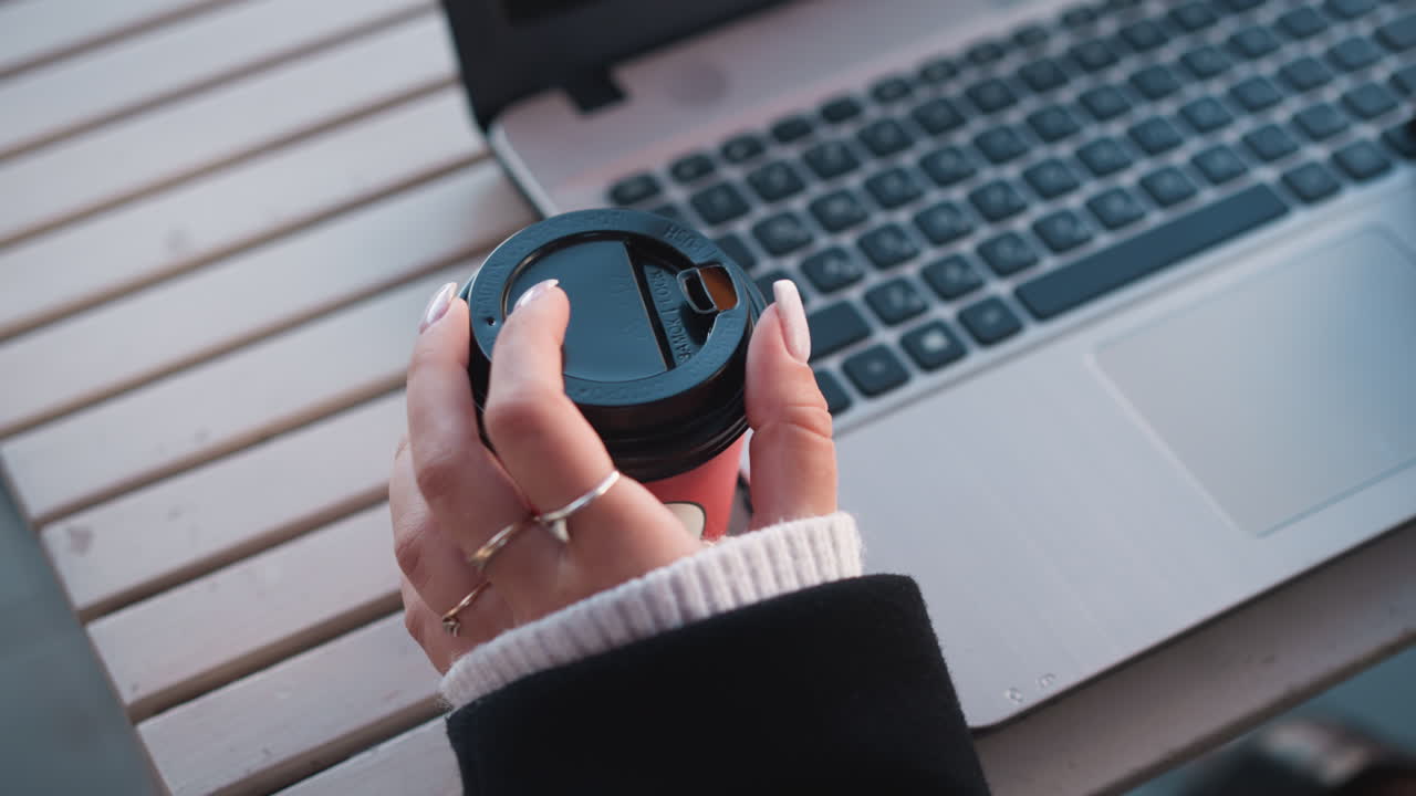 primer plano de la mano de una dama girando suavemente una taza de café cerca de una computadora portátil, destacando sus dedos cuidados contra el teclado de la laptop en un entorno profesional