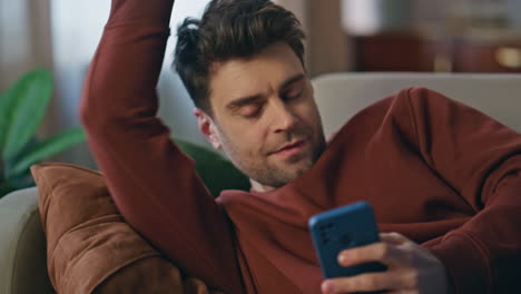 bored man browsing mobile phone app lying couch close up. guy looking smartphone