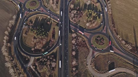 a drone-captured video of a highway with two large roundabouts surrounded by green spaces and trees. flying over the moving cars and trucks on the highway.