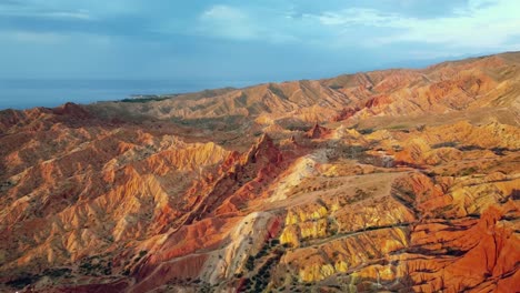 Drone-flying-over-red-canyon-mountains-at-sunset,-capturing-rugged-peaks,-and-stunning-colours-reflecting-on-the-lake,-with-stormy-clouds-adding-a-dramatic-touch