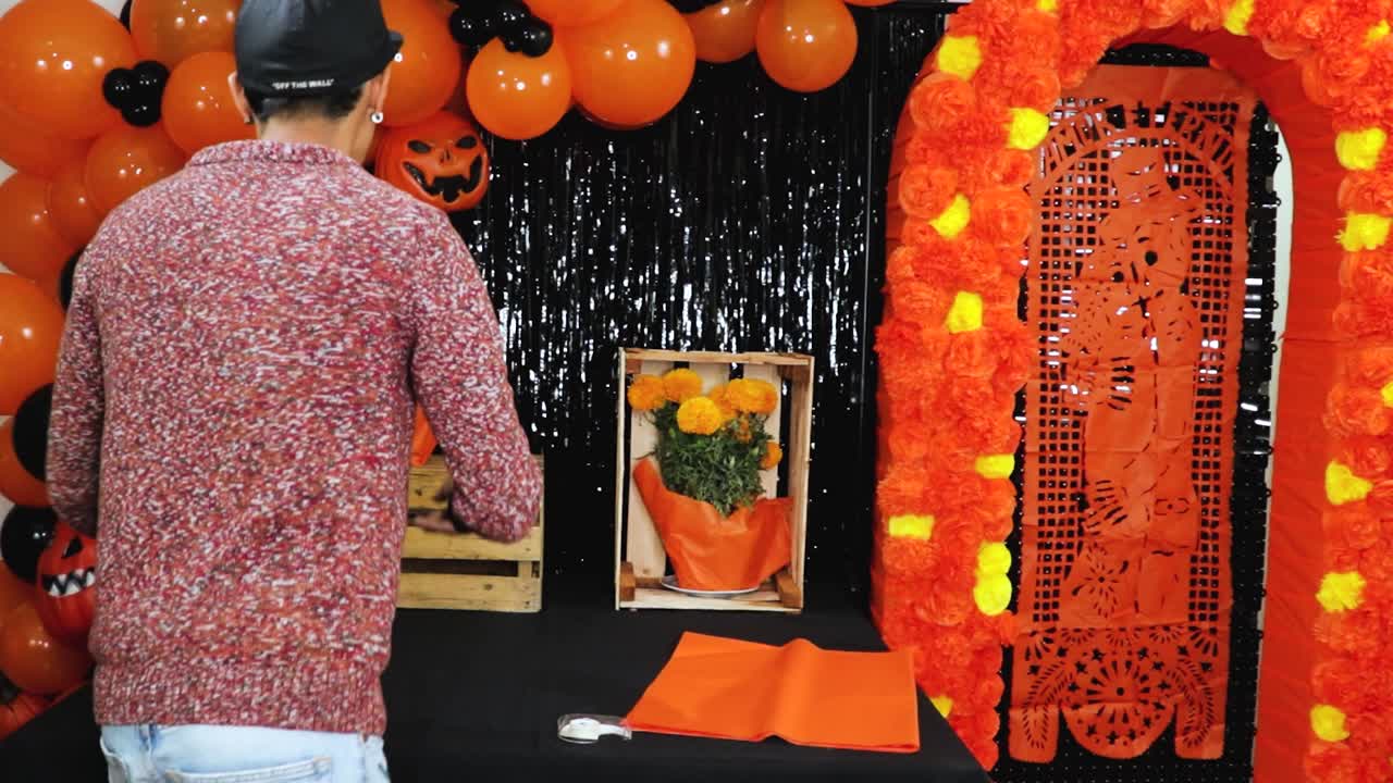 hombre latino decorando el altar de halloween con flores de cempasuchil naranja