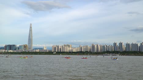 people kayaking and paddle boarding in han river in seoul, south korea with the lotte world tower dominating the city skyline