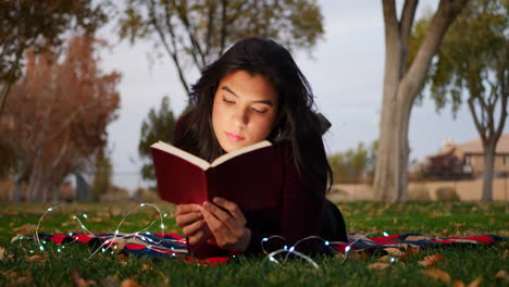 Eine-Junge-Erwachsene-Frau,-Die-Ein-Buch-Liest-Und-Ihre-Fantasie-Einsetzt,-Um-Die-Geschichte-Draußen-Im-Park-Bei-Sonnenuntergang-Zum-Leben-Zu-Erwecken