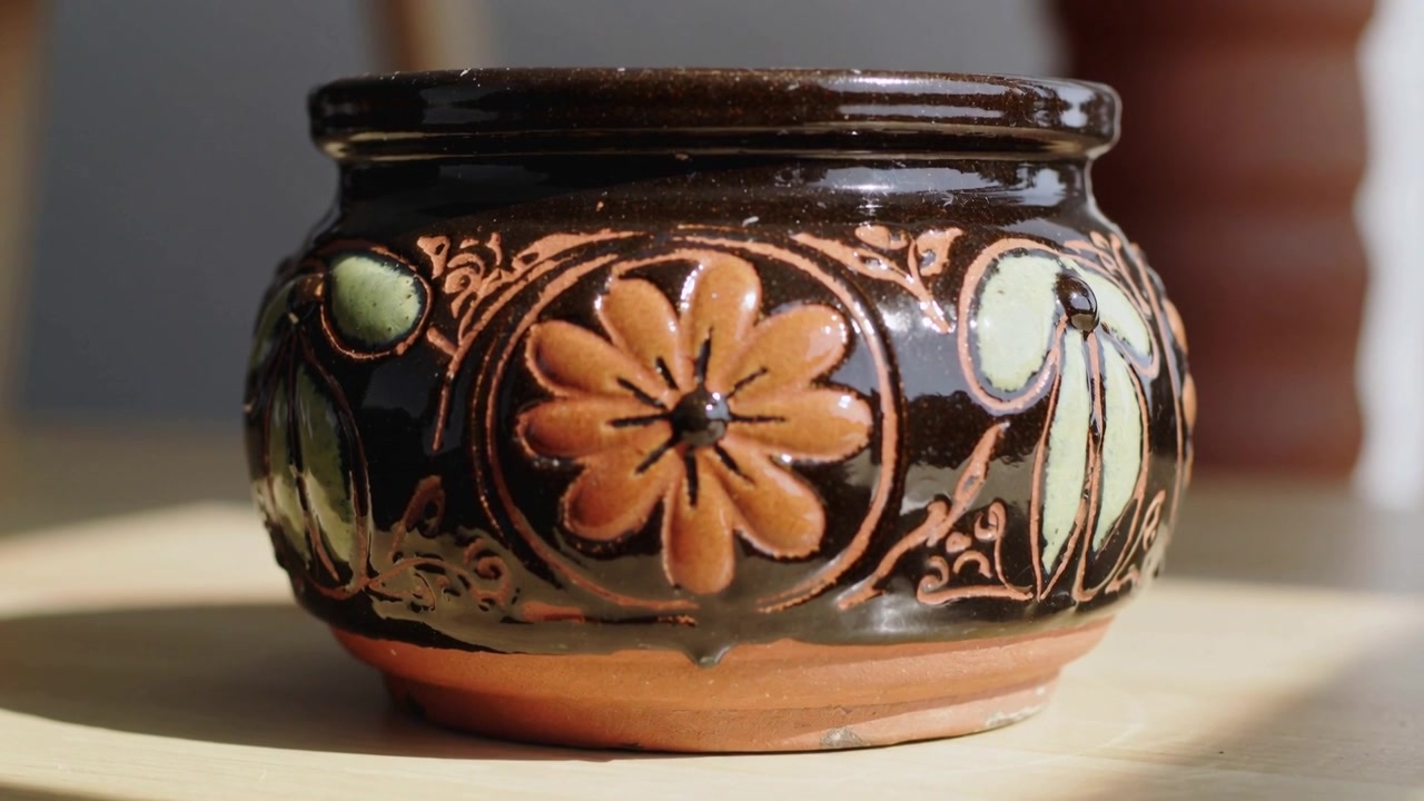 Telecamera che zooma e si concentra su un vaso di ceramica a tavola vicino alla finestra, l'operatore inizia lo zoom rivelando la smaltatura