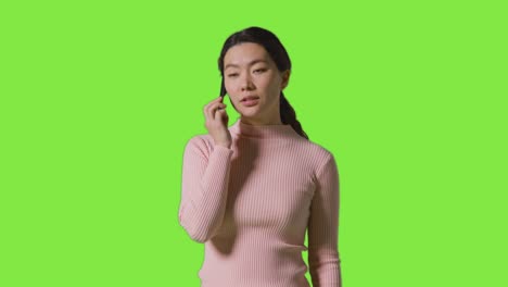 studio shot of woman answering mobile phone and getting good news against green screen