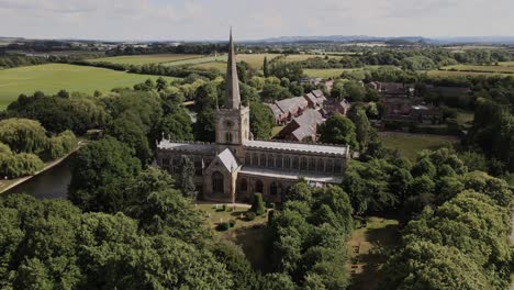 Holy-Trinity-church-orbiting-aerial-view-across-lush-green-rural-Warwickshire-countryside