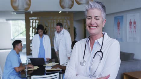 retrato de una doctora caucásica sonriendo, con colegas en discusión en el fondo